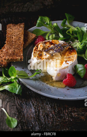 Tranches de fromage de chèvre fondante grillé sur plaque bleue, servi avec du miel liquide, de lavande, de framboises, de farine de pain grillé et sa verte Banque D'Images