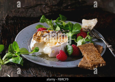 Tranches de fromage de chèvre fondante grillé sur plaque bleue, servi avec du miel liquide, de lavande, de framboises, de farine de pain grillé et sa verte Banque D'Images