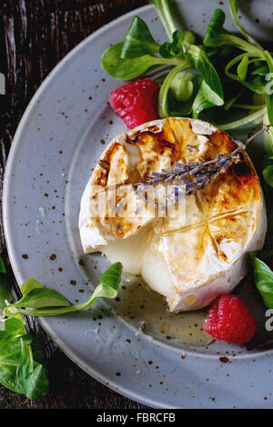 Tranches de fromage de chèvre fondante grillé sur plaque bleue, servi avec du miel liquide, de lavande, de framboises, de farine de pain grillé et sa verte Banque D'Images