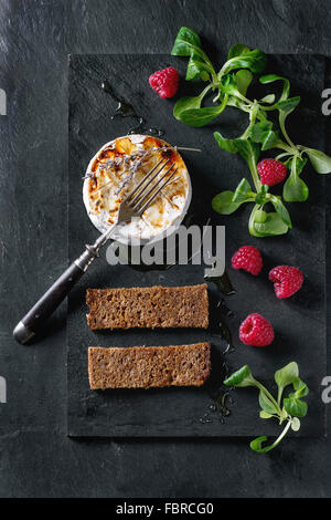 Fromage de chèvre grillé servi sur ardoise noire avec du miel liquide, lavande, framboise, de farine de pain grillé et salade verte. Avec Banque D'Images