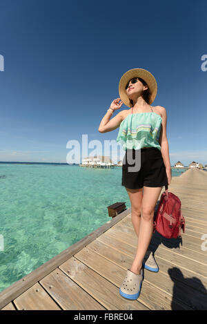 Slim woman wearing hat et lunettes affichage sur pont de bois sur la claire eau de mer à Maldives sur une journée ensoleillée Banque D'Images