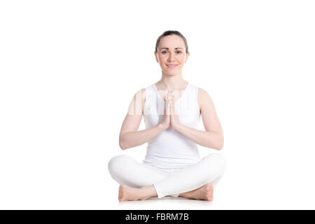 Belle sportive souriante jeune femme en blanc sportswear assis dans facile, Sukhasana posent avec les mains dans l'asana, Namaste Banque D'Images