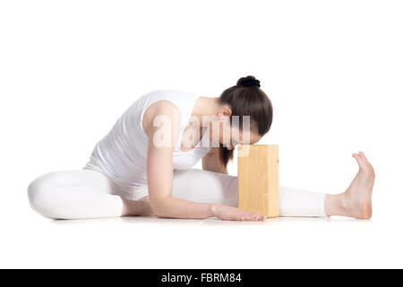 Belle jeune sportif yoga début élève de sportswear blanc assis dans la tête à l'avant du genou bend posent leaning on wooden Banque D'Images