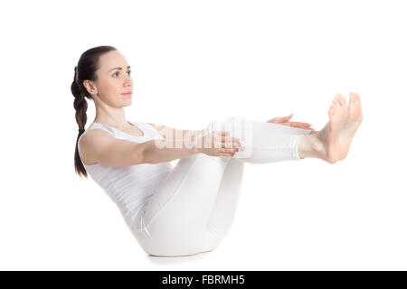 Belle jeune femme sportive en blanc sportswear faisant des exercices pour le dos, les hanches et les muscles abdominaux, assis dans navasana Banque D'Images