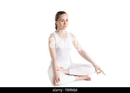 Belle jeune femme sportive en blanc sportswear sitting cross legged, dans Ardha Padmasana, méditer, faire des exercices de respiration Banque D'Images