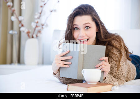 Heureux surpris charmante jeune femme couchée sur le lit et le livre de lecture dans la chambre Banque D'Images