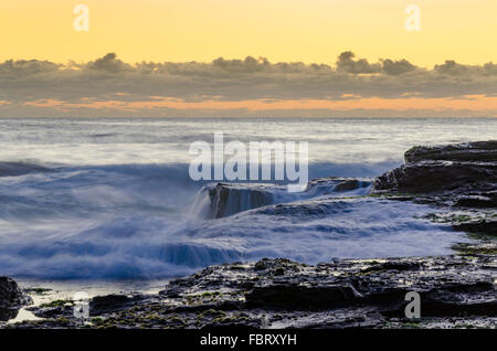 Les vagues débordent sur le bord d'une plate-forme rocheuse tandis que le soleil se lève sur une plage de Sydney en Australie Banque D'Images