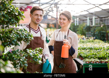 Heureux l'homme et de la femme, les pépiniéristes holding arrosoir et pulvérisateur pour la pulvérisation des fleurs et plants in greenhouse Banque D'Images