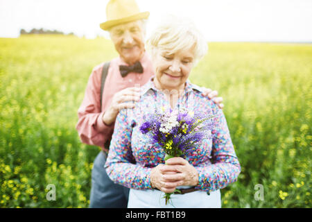 Happy senior femme avec bouquet de fleurs sauvages et son mari derrière Banque D'Images