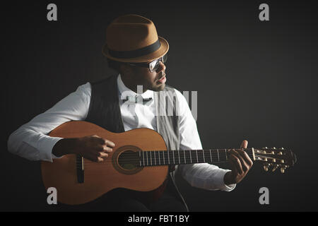 Jeune homme élégant en vêtements intelligents et hat playing guitar Banque D'Images