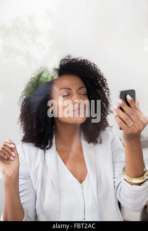 Woman blowing kiss at smartphone tout en faisant du chat vidéo Banque D'Images