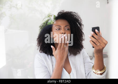 Woman blowing kiss at smartphone tout en faisant du chat vidéo Banque D'Images