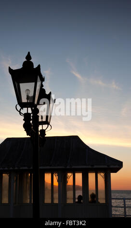 Deux personnes assis dans un abri d'ornement regarder le coucher de soleil sur la jetée de Cromer, cromer, Norfolk, Angleterre, Royaume-Uni Banque D'Images