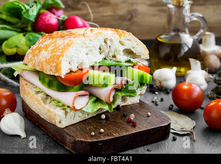 Sandwich au jambon et légumes avec du pain frais sur une planche à découper en bois Banque D'Images