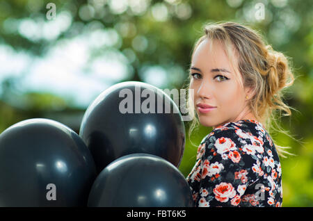 Belle hispanique model wearing summer dress posing for camera avec noir de ballons, angle profil Banque D'Images