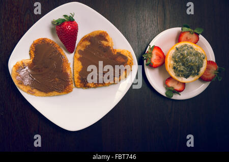 Crêpes Heartshaped recouvert de chocolat et fraise à côté de barbadine entouré par couper les fraises, vu de dessus, le petit-déjeuner élégant concept Banque D'Images