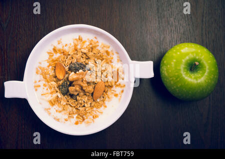 Le yogourt avec granola, raisins secs et une pomme qui est assis à côté de bol, vu de dessus, le petit-déjeuner élégant concept Banque D'Images