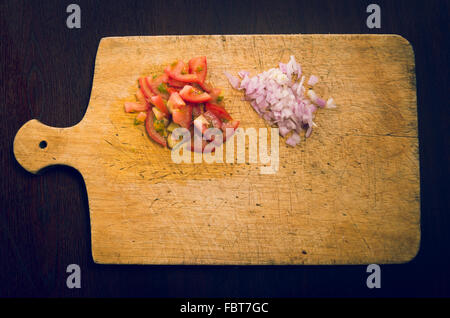 Planche à découper en bois avec des morceaux de tomates et d'oignons, comme vu de dessus Banque D'Images