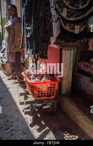 Un lave-linge en plastique rouge panier plein d'accessoires pris dans un éclat de lumière. L'habillement femelle propriétaire de boutique supervise ses marchandises. Banque D'Images