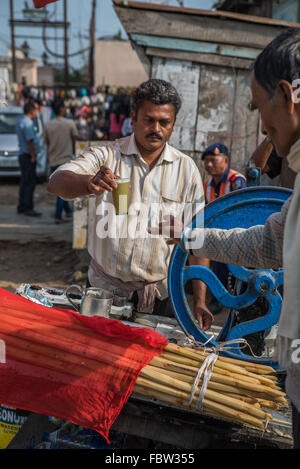 Canne à sucre routière wallah / vendeur de remettre un verre de jus de canne à sucre et de verre à un client. Banque D'Images