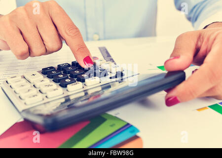 Une femme d'affaires à l'aide d'un calculateur électronique dans son bureau, avec un bureau plein de graphiques Banque D'Images
