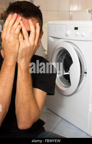 Jeune homme malheureux avec lave linge Banque D'Images