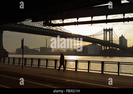 Un homme marche sur le nord de l'East River Esplanade que le soleil se lève sur le Manhattan Bridge enjambant l'East River, NEW YORK Banque D'Images