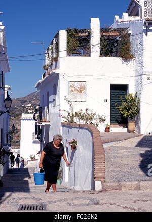 Vieille Dame vêtue de noir traditionnel portant un seau d'un village-rue étroite, Frigiliana, la province de Malaga, Espagne. Banque D'Images