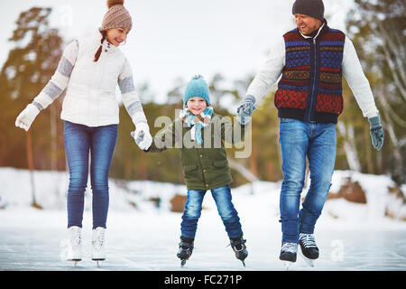 Happy boy holding de ses parents par les mains si le patinage sur la patinoire Banque D'Images