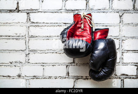 Ancienne Paire de gants de boxe rouge et noir accroché sur un mur de briques blanches. Banque D'Images