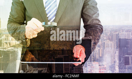 Image composite de businessman looking at tablet avec loupe Banque D'Images