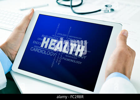 Libre d'un médecin homme assis à son bureau 24 holding a tablet computer avec un nuage de tags à propos de la santé dans son écran Banque D'Images