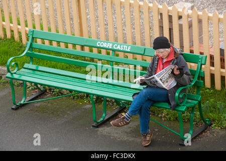 Femme assise sur un banc à Corfe Castle gare lire le journal Daily Echo en Décembre Banque D'Images
