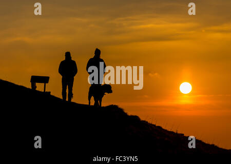 Camp Bratton, Westbury White Horse, Wiltshire, Royaume-Uni. Le 20 janvier, 2016. Météo britannique. Un magnifique coucher du soleil orange jette dog walkers en bravant le silhouette, sous-glace conditions zéro sur la colline surplombant la ville de Westbury ci-dessous. L'ancien site du patrimoine anglais exposés abrite le célèbre cheval blanc craie et de gravure a été couvert dans une couverture de givre pour une bonne partie de la journée. Credit : Wayne Farrell/Alamy Live News Banque D'Images