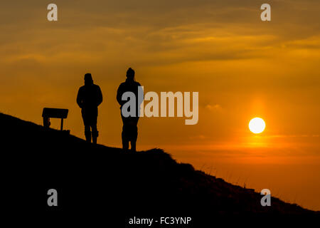Camp Bratton, Westbury White Horse, Wiltshire, Royaume-Uni. Le 20 janvier, 2016. Météo britannique. Un magnifique coucher du soleil orange jette les marcheurs en bravant le silhouette, sous-glace conditions zéro sur la colline surplombant la ville de Westbury ci-dessous. L'ancien site du patrimoine anglais exposés abrite le célèbre cheval blanc craie et de gravure a été couvert dans une couverture de givre pour une bonne partie de la journée. Credit : Wayne Farrell/Alamy Live News Banque D'Images