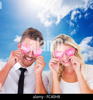 Composite image of young couple holding coeurs roses au-dessus des yeux Banque D'Images