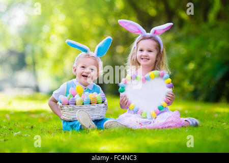 Petit garçon et fille s'amusant sur chasse aux œufs de Pâques. Kids in Bunny Ears et costume de lapin. Les enfants avec des oeufs colorés Banque D'Images