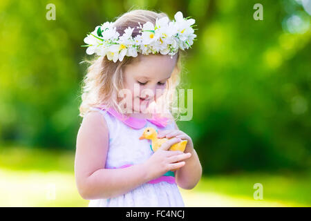 Petite fille s'amusant sur chasse aux œufs de Pâques. Kid en jouant avec la couronne de fleurs canard ou poulet. Banque D'Images