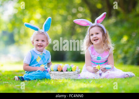 Petit garçon et fille s'amusant sur chasse aux œufs de Pâques. Kids in Bunny Ears et costume de lapin. Les enfants avec des oeufs colorés Banque D'Images