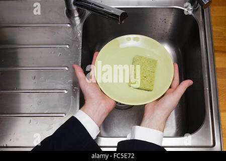 Nettoyer la plaque de fond sur l'évier de cuisine dans les mains d'un homme en costume Banque D'Images
