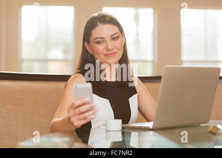 Hispanic businesswoman using cell phone in office Banque D'Images