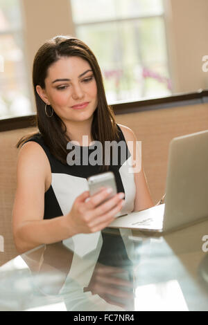 Hispanic businesswoman using cell phone in office Banque D'Images