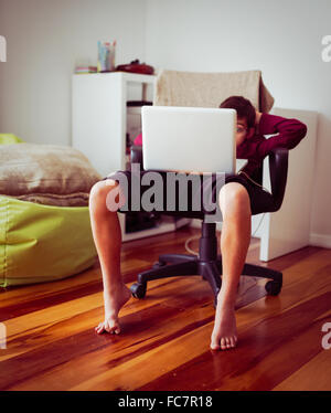 Mixed Race boy using laptop in chair Banque D'Images