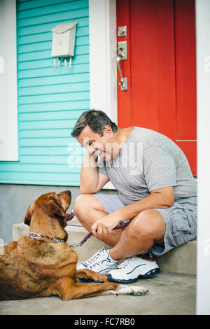 Caucasian man petting dog in front stoop Banque D'Images