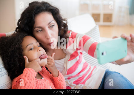 Mère et fille en tenant sur canapé selfies Banque D'Images