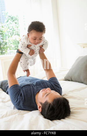 Père holding baby son on bed Banque D'Images