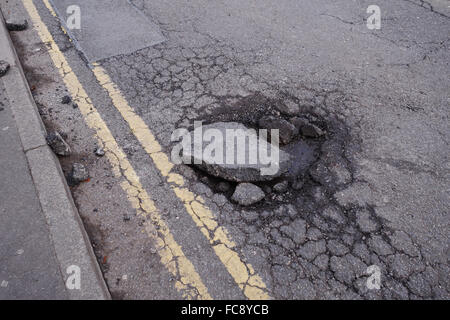 Un grand pothole dans une route de tarmac à côté de double jaune sans file d'attente, Stoke-on-Trent, Staffordshire, Angleterre, Royaume-Uni Banque D'Images