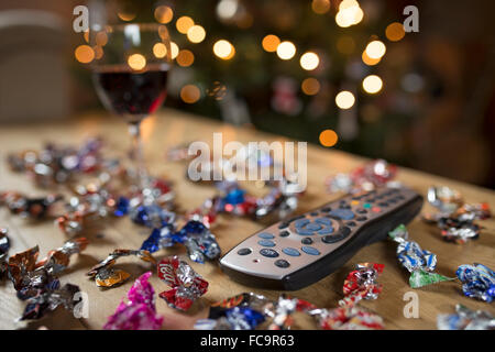 Télécommande du téléviseur entouré de bonbons et un verre de vin rouge à Noël. Banque D'Images