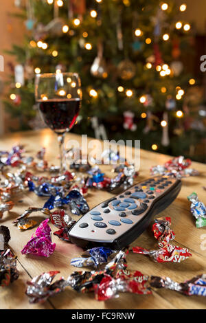 Télécommande du téléviseur entouré de bonbons et un verre de vin rouge à Noël. Banque D'Images