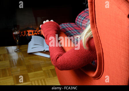 Dame en jouets confortable de détente dans un fauteuil près de la cheminée avec un verre de vin et des livres à côté Banque D'Images